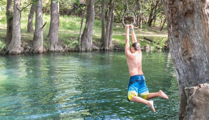 Child swinging into Blue Hole Swimming Hole in Wimberly Texas