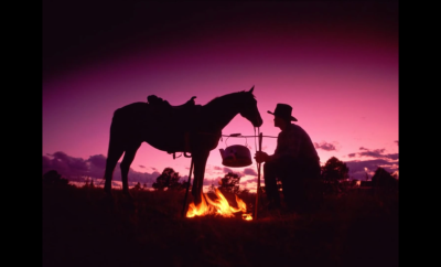 Silhouette of cowboy and his horse in front of a campfire at sunset