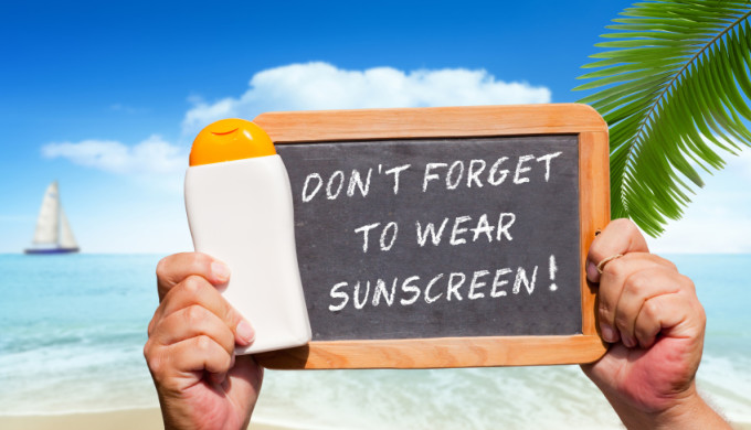 Human Hands hold a bottle sunscreen and a slate blackboard with text message "Don´t forget to wear Suncreen"